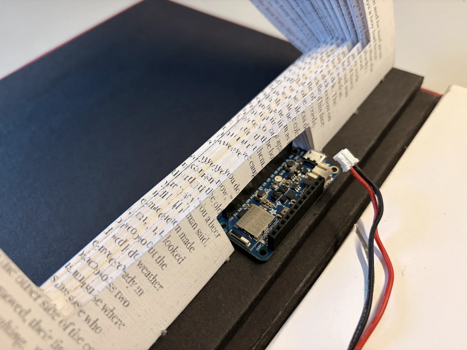 Close-up of the Arduino Feather fixed into the book's spine beside the edges of the pages