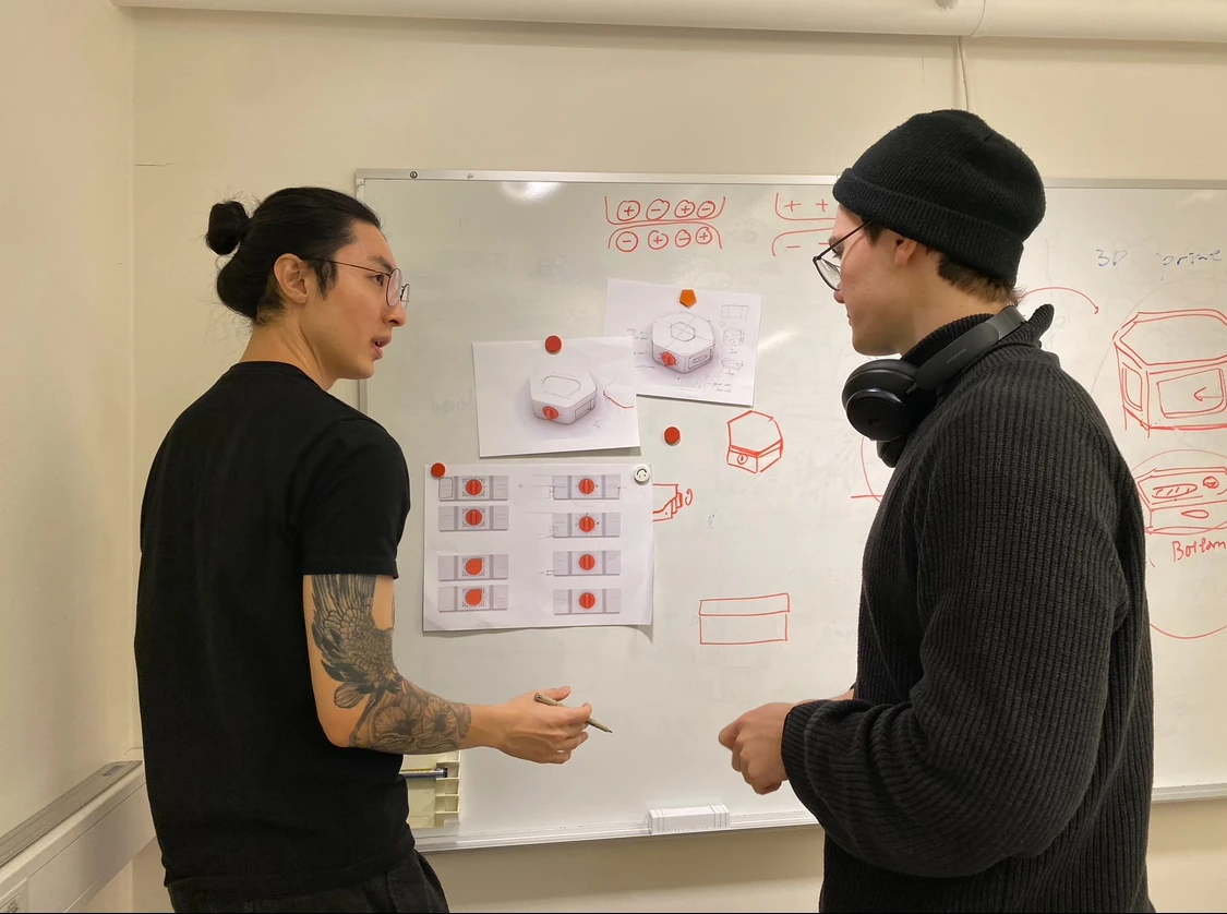 Two team members discussing sketches of the base at a whiteboard