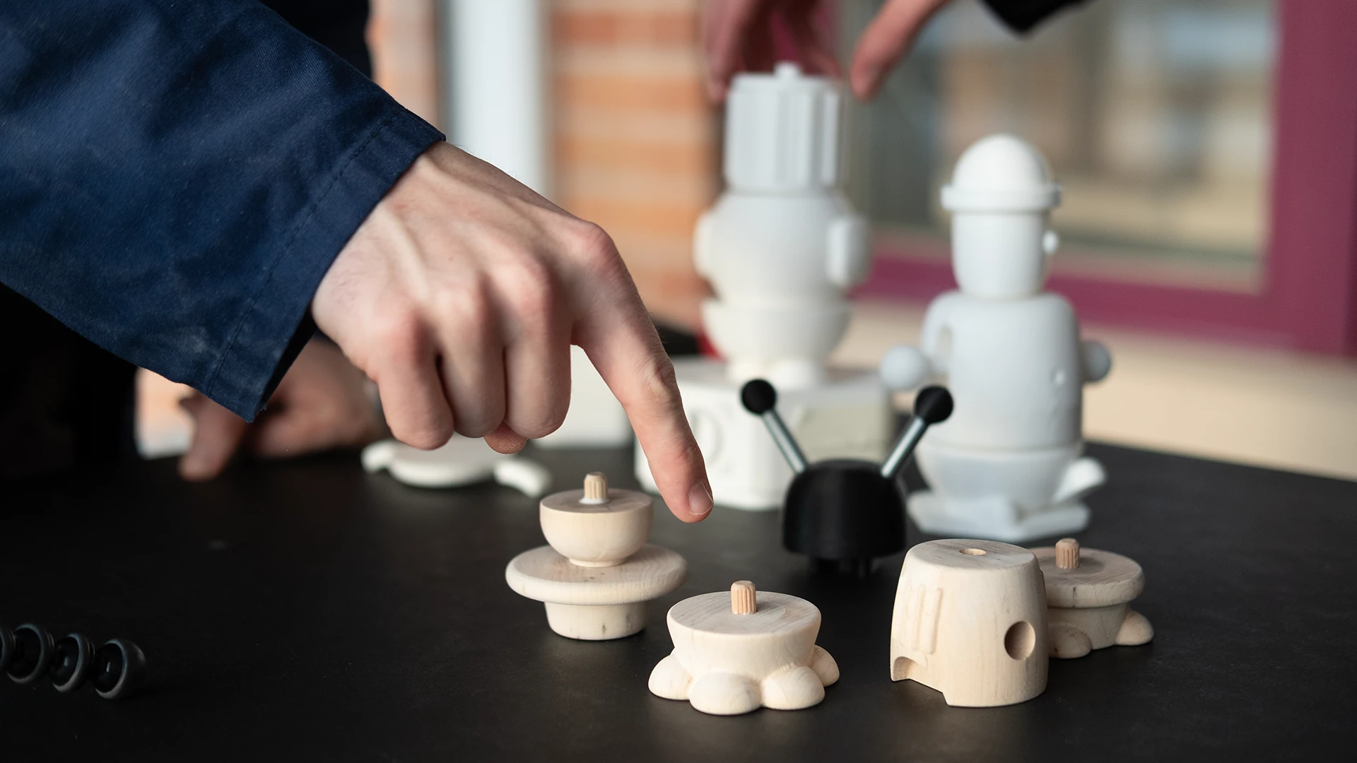Pointing at wooden module prototypes in front of 3D-printed ones